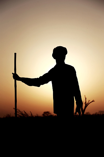 Silhouette of a farmer holding fork (agriculture tool) on his shoulder during sunset.