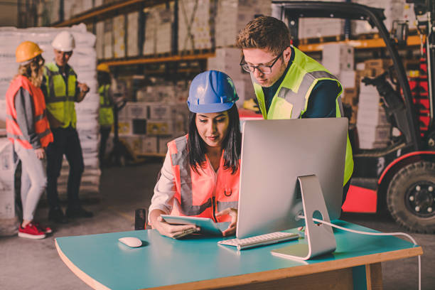 Business colleagues working with tablet computer in warehouse Young warehouse worker businessman and businesswoman working and looking at tablet and desk computer in a large warehouse warehouse office stock pictures, royalty-free photos & images