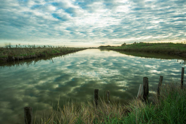 sunset on a chennel inside the Po river lagoon with some wood fences in foreground