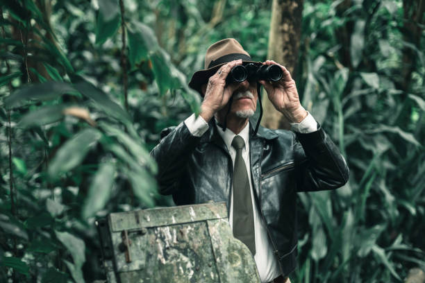 istock Explorer looking with binoculars standing in bush next to car wreckage. 686254316