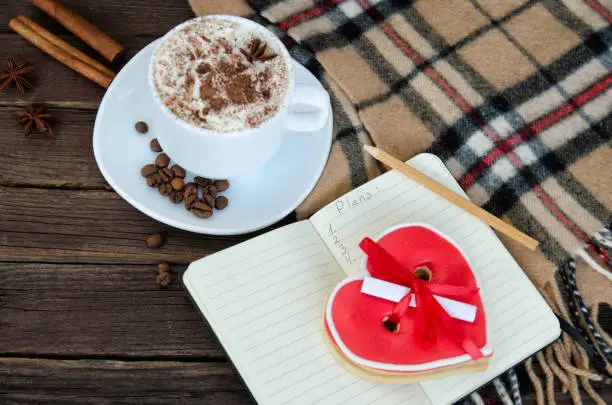 Cozy rest. Mug latte, notepad with pencil, gingerbread-heart, plaid plaid and coffee beans. Top view