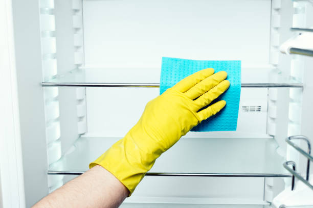 istock Man's hand in yellow gloves washing refrigerator inside with blue duster 686261072