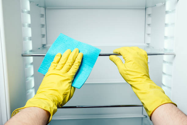 istock Man's hand in gloves cleaning white fridge with blue rag at kitchen 686261106