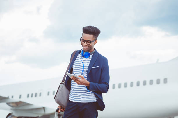 jeune homme d’affaires à l’aide d’une tablette numérique en face de l’avion - airport passengers photos et images de collection