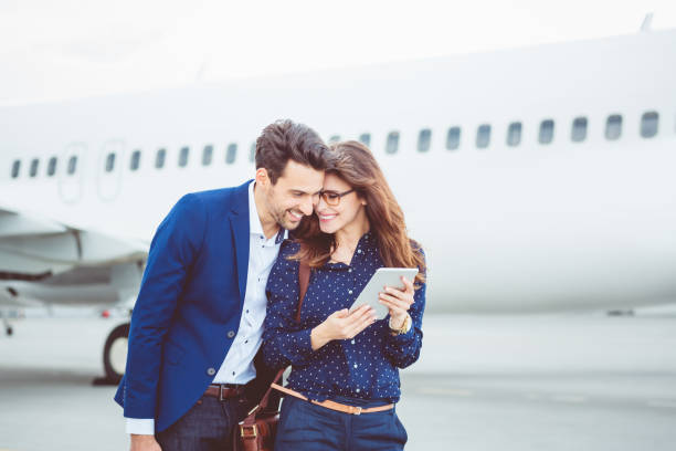 Loving couple with a digital tablet in front of airplane