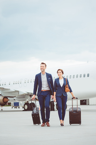 Full length shot of businessman and businesswoman walking together at the airport. Business people walking in front of the airplane with luggage.
