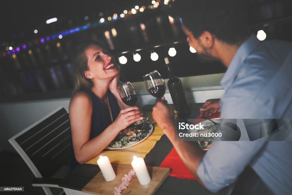 Young beautiful couple having romantic dinner on rooftop Young beautiful couple in love having romantic dinner at night on rooftop Couple - Relationship Stock Photo