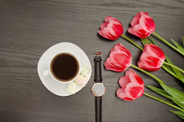 istock Mug with coffee, watch, pink tulips. Black table. Top view 686281510