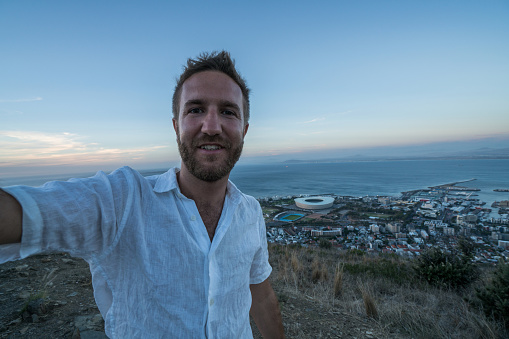 Cheerful young man in Cape Town, South Africa taking selfie portrait at sunrise. People technology lifestyle concept.