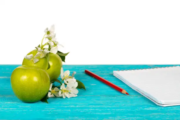 apple and apple tree blossoms on a wooden turquoise table with notebook and red pencil
