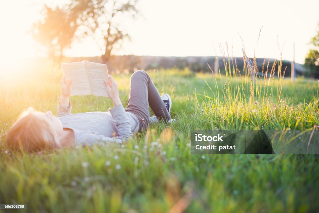 Girl reading a book outside header Young girl reading a book in the grass while sun setting down. Summer feeling. Reading Stock Photo