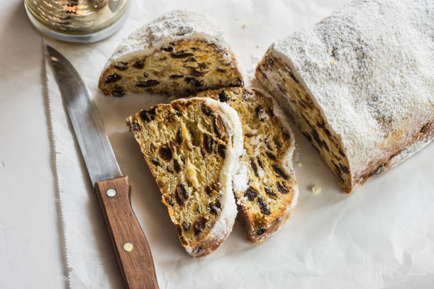 istock German Christmas stollen with cut off slices on parchment paper, white concrete background, knife, lit candle, minimalist style, top view 686312368