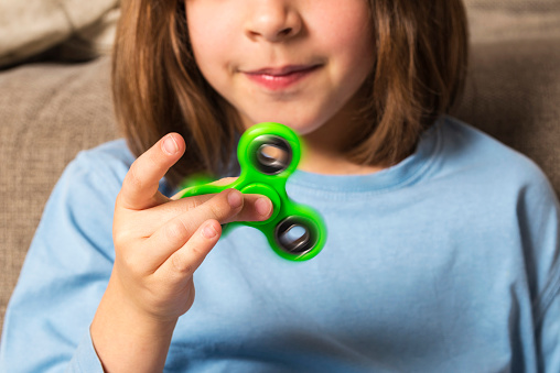 Little girl playing with green fidget spinner toy to relieve stress at home