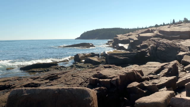 CLOSE UP: North Atlantic Ocean swashing rocky coastline in Maine on sunny day
