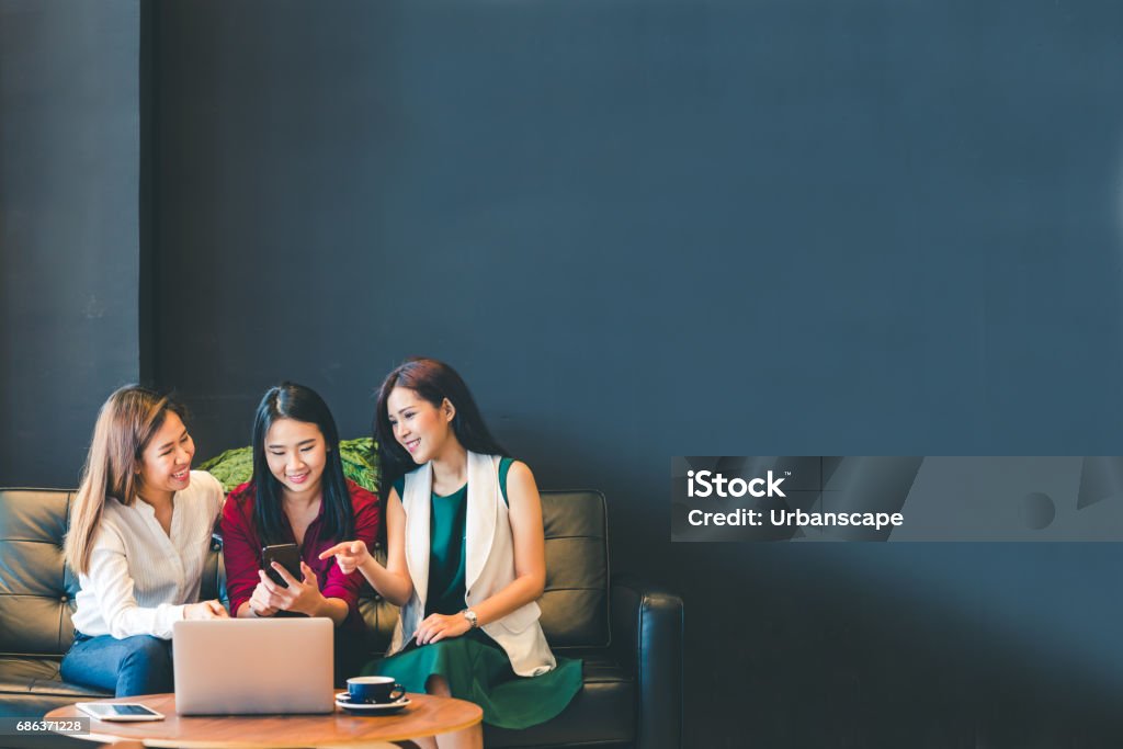 Três lindas garotas asiáticas usando smartphone e laptop, conversando sobre o sofá no café com espaço de cópia, estilo de vida moderno com tecnologia gadget ou mulher trabalhadora no conceito de negócios casuais - Foto de stock de Amizade royalty-free