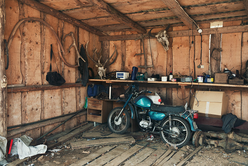 Old motorcycle in a wooden picturesque barn, with a lot of different objects and all rubbish