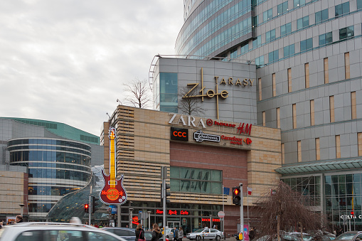 People walk in front of modern commercial, office, and entertainment complex in the city center with Hard Rock Cafe and Shopping Mall Zlote Tarasy.