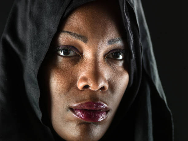 Beauty portrait of brunette woman dressed in dark blue scarf. Female portrait from a three-quarter angle on black background. Hand wraps the scarf.