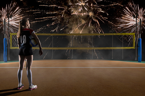 Female volleyball player holding the ball on volleyball night field with fireworks on background