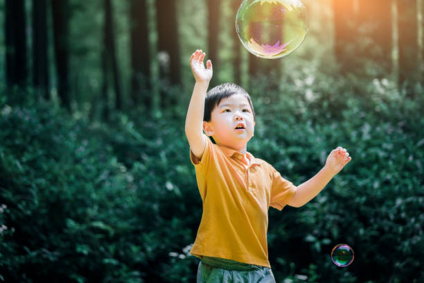 Cheerful toddler boy playing with soap bubbles in park