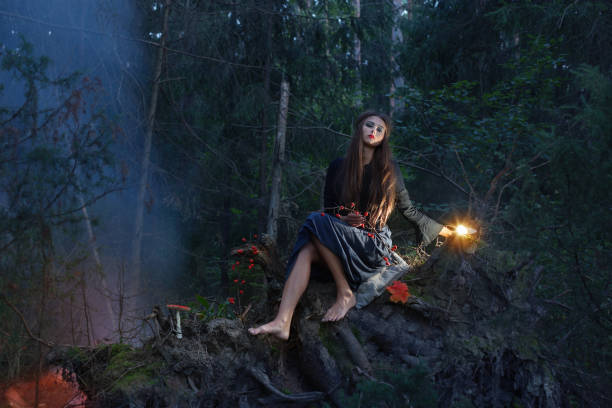 istock Beautiful witch sitting on a tree trunk in the forest 686435970