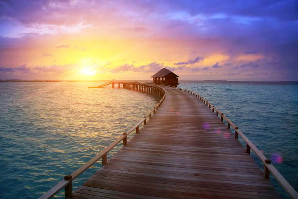 wooden road from the island to a hut over water on a sunset. Maldives. stock photo