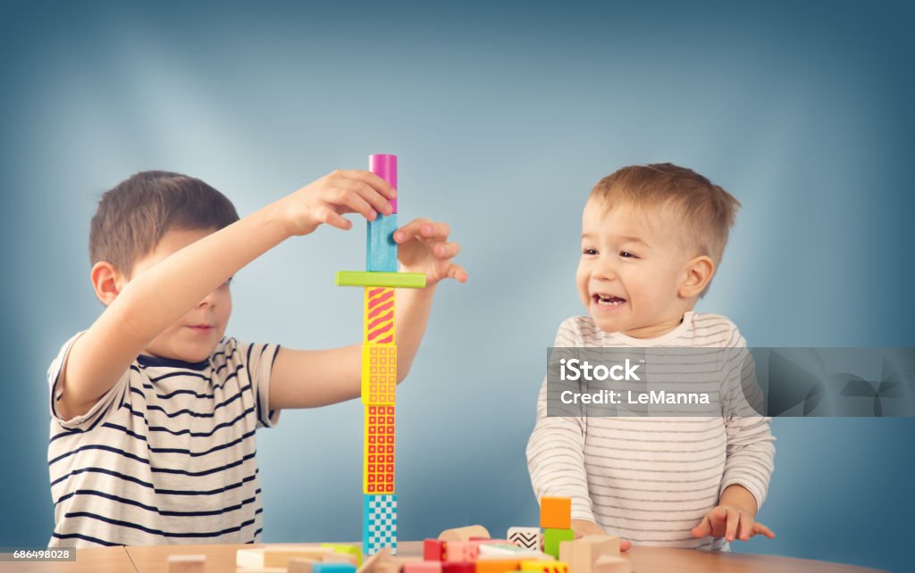 Portrait of a two years old child sitting at the table Portrait of a two years old child stacking wooden cubes. Pretty little boy on blue background Assistance Stock Photo