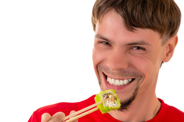 istock smiling young man eating green sushi roll 686511628