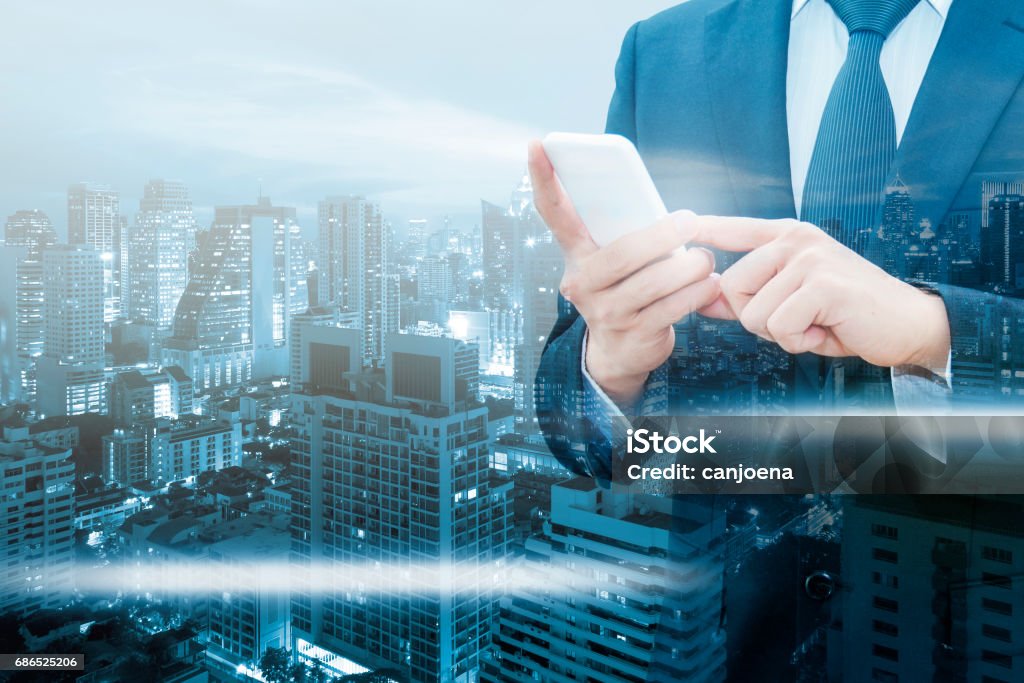 Double exposure of professional businessman using smart phone and network connection with city of business background in communication & Business trading concept Adult Stock Photo