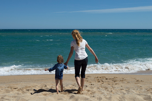 Mother and son having fun on the beach. They are running through the waves. Happy sunny day.