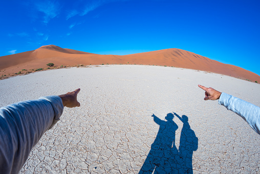 Fingers pointing to the scenic sand dunes of Sossusvlei, Namib Naukluft National Park, Namibia, Africa. Adventure and exploration in Africa, concept of people traveling around the world. Fish eye view.