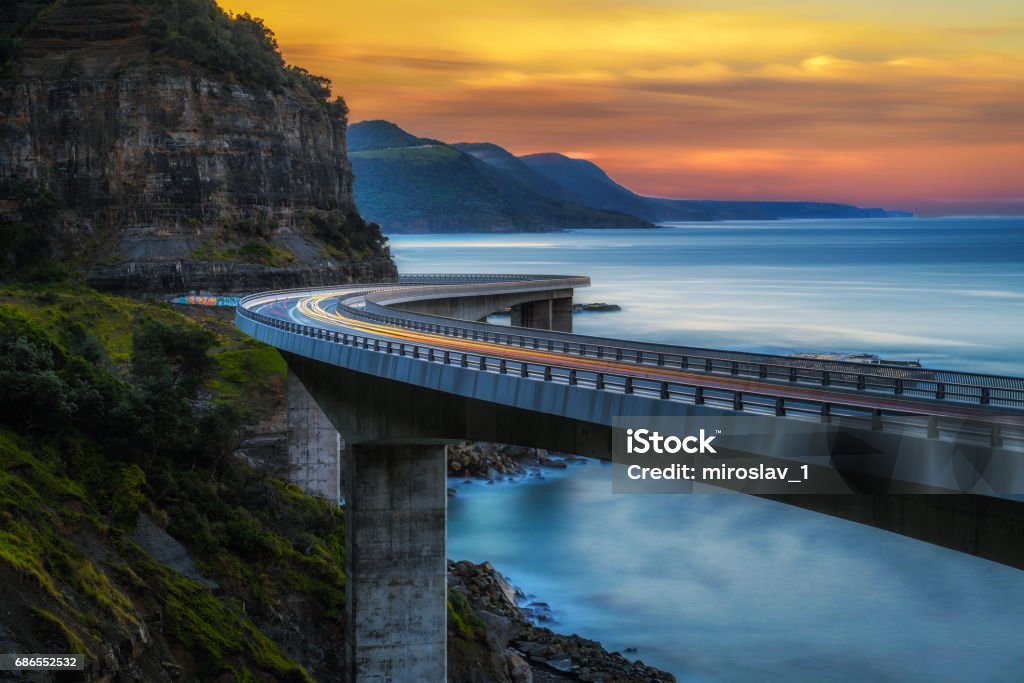 Coucher de soleil sur le pont de falaise de mer le long de la côte de l’océan Pacifique australien avec les lumières des voitures qui passent - Photo de Pont libre de droits