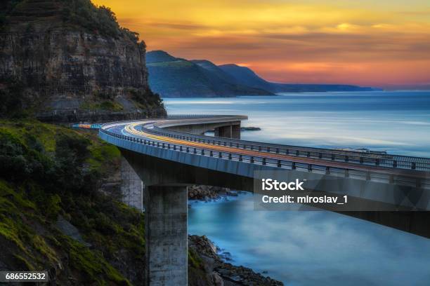 Sunset Over The Sea Cliff Bridge Along Australian Pacific Ocean Coast With Lights Of Passing Cars Stock Photo - Download Image Now