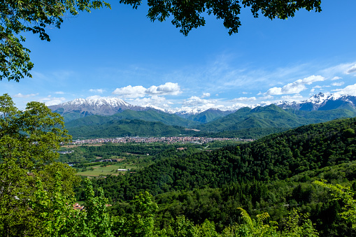 South view of piedmontese alps with snowy mountains and woods in spring from the Sanctuary of Madonna degli Alpini, in Cervasca, Cuneo, Italy. The town of Borgo San Dalmazzo is also visible.