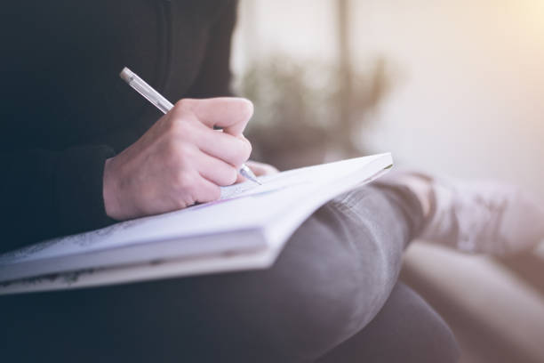 mujer escribiendo o garabateando en un bloc de notas que descansa sobre sus piernas - diary writing women human hand fotografías e imágenes de stock