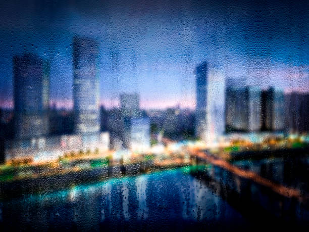 Digitally generated rain drops on window with defocused tall urban buildings in the background.