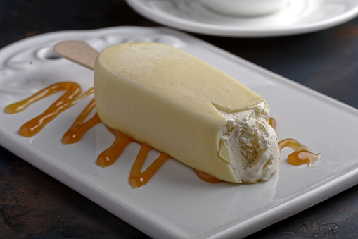 Ice cream bar coated with white chocolate on a ceramic cutting board