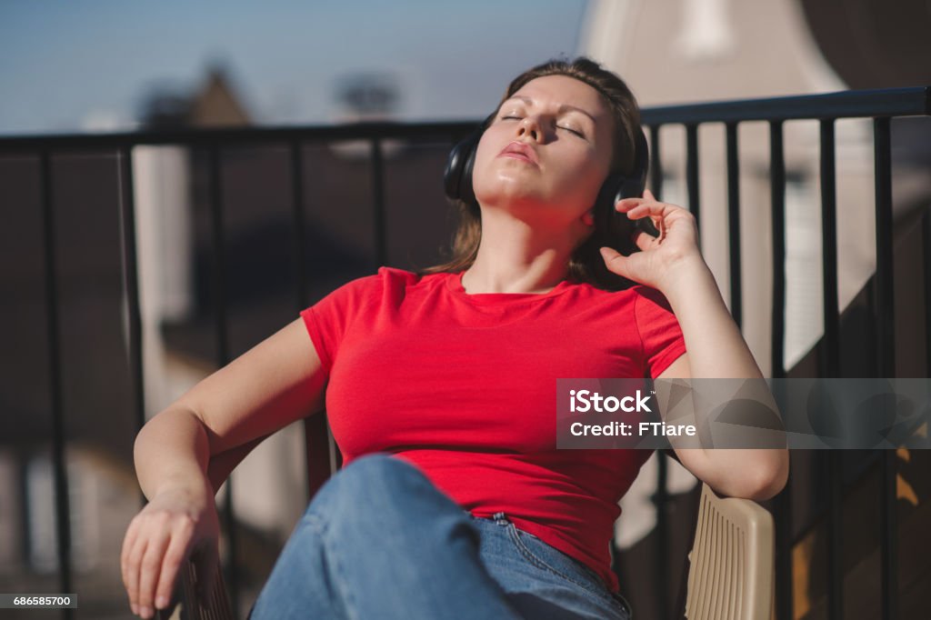 Beautiful girl in a red t-shirt and headphones. A girl on the balcony listening to music and is singing Beautiful female in a red t-shirt and headphones. A girl on the balcony listening to music and is singing Adult Stock Photo