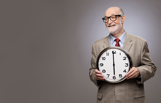 Studio portrait of a senior man holding a big wall clock on gray background with copy space