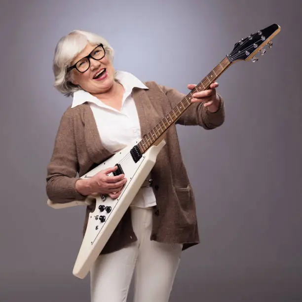 Happy funny senior woman playing electric guitar