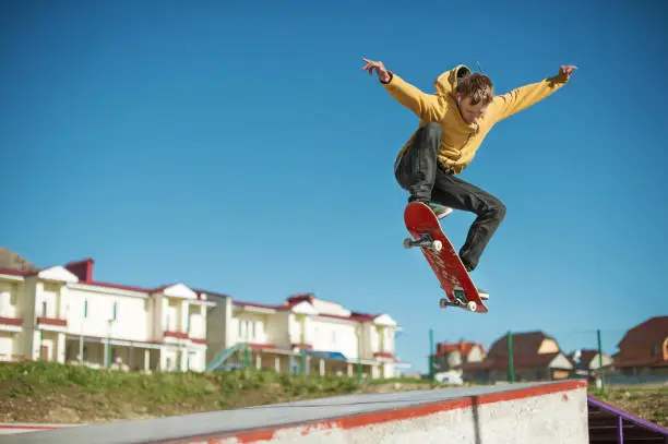 A teenager skateboarder does an ollie trick in a skatepark on the outskirts of the city On a background of houses and a blue sky