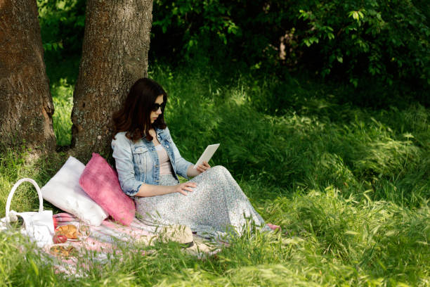 heure d’été. jeune femme à un pique-nique lire un e-book. - women grass glasses e reader photos et images de collection