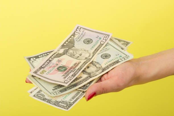 istock Fifty, twenty, five and one dollars in the woman's hand, yellow background 686606762