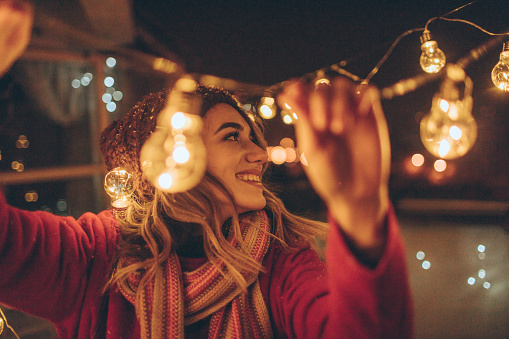 Photo of a young woman who is hosting New Year's party and having the last preparations on the venue - charming balcony over the city