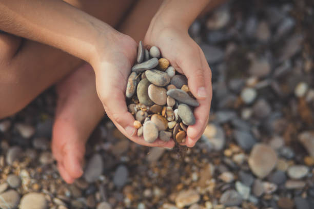 Woman hands holding small stones in hands on beach background with burning sun.