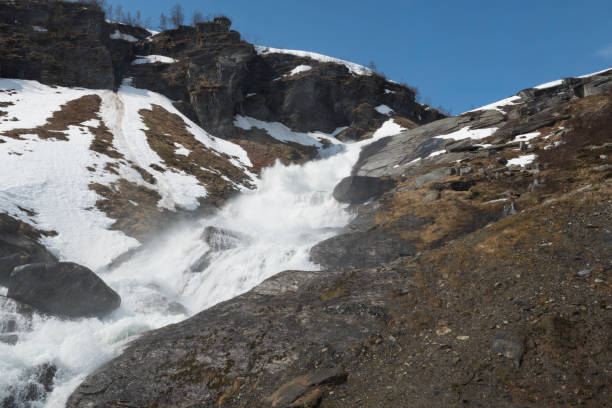 Snow and ice are melting in the mountains of Norway in spring resulting in a lively stream of water (or small river) with a waterfall. The image was captured near Myrkdalen at mid/late May. Myrkdalen is a snow-rich area with tracks and slopes, cabins, hotels and resorts popular with all kinds of skiers and snowboarders situated in the municipality of Voss in the county of Hordaland in Norway. National Road 13  runs from the town of Sandnes in Rogaland county to the municipality of Balestrand in Sogn og Fjordane county and passes this area.