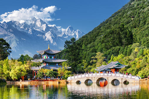 Amazing view of the Jade Dragon Snow Mountain and the Black Dragon Pool, Lijiang, Yunnan province, China. The Suocui Bridge over pond and the Moon Embracing Pavilion in the Jade Spring Park.