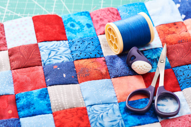 istock Scissors, thread and thimble lying on blue and red square pieces of fabric sewn together 686685444