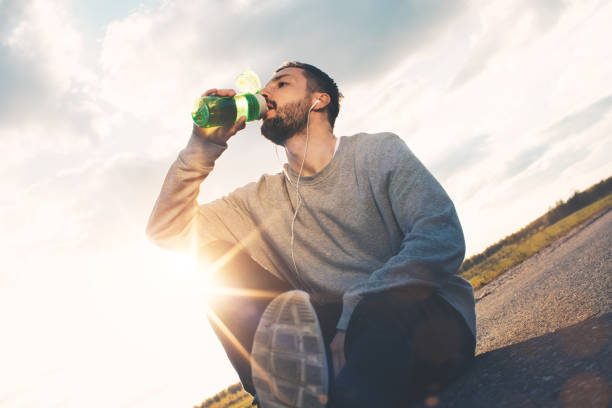 istock Athlete drinks water while sitting on the asphalt and resting after workout outdoors in the park 686702184