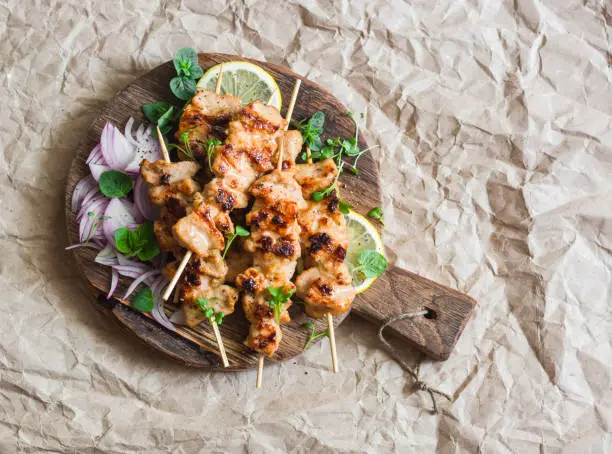 Photo of Grilled pork skewers with pickled red onion and mint on a rustic cutting board on a paper background. Delicious summer lunch. Healthy food concept